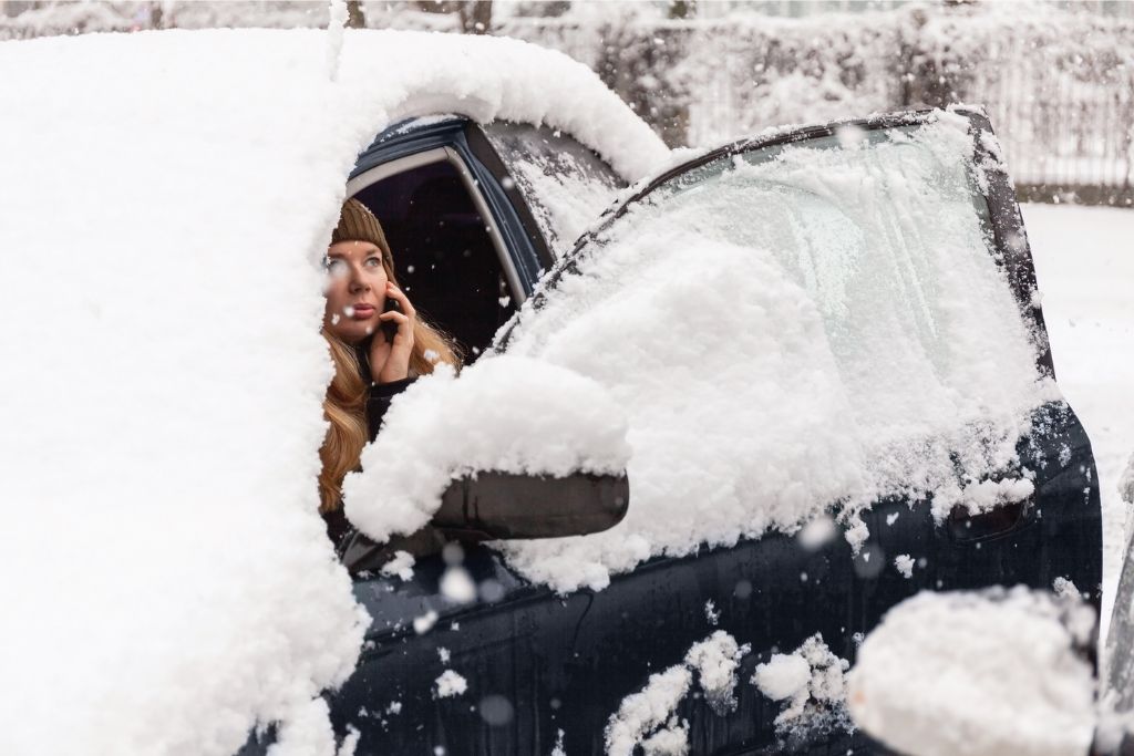 Woman on the phone sitting in her car covered in snow 