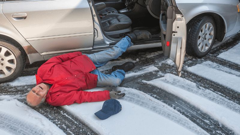 Man on snowy/icy ground next to car with door open