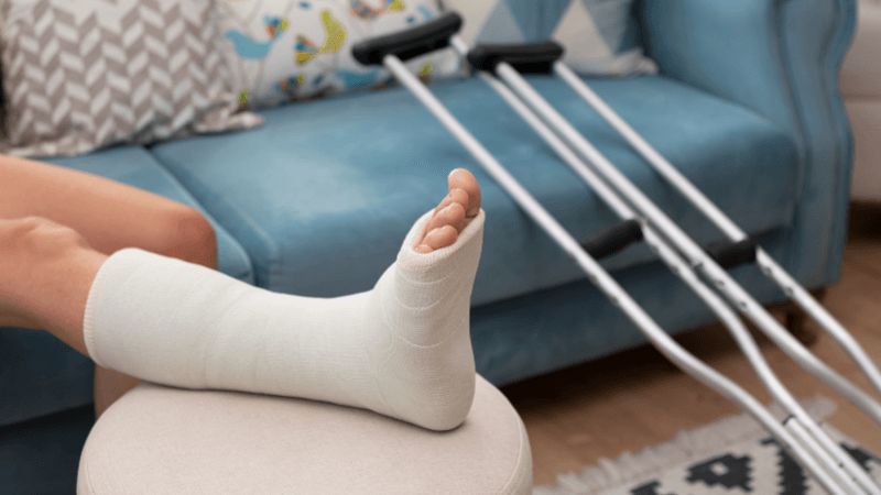 Right foot and leg in cast with crutches leaning on couch nearby