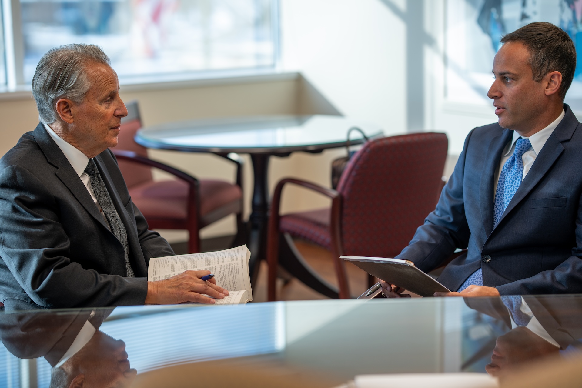 Two businessmen in formal attire having a meeting in an office setting, discussing business documents.
