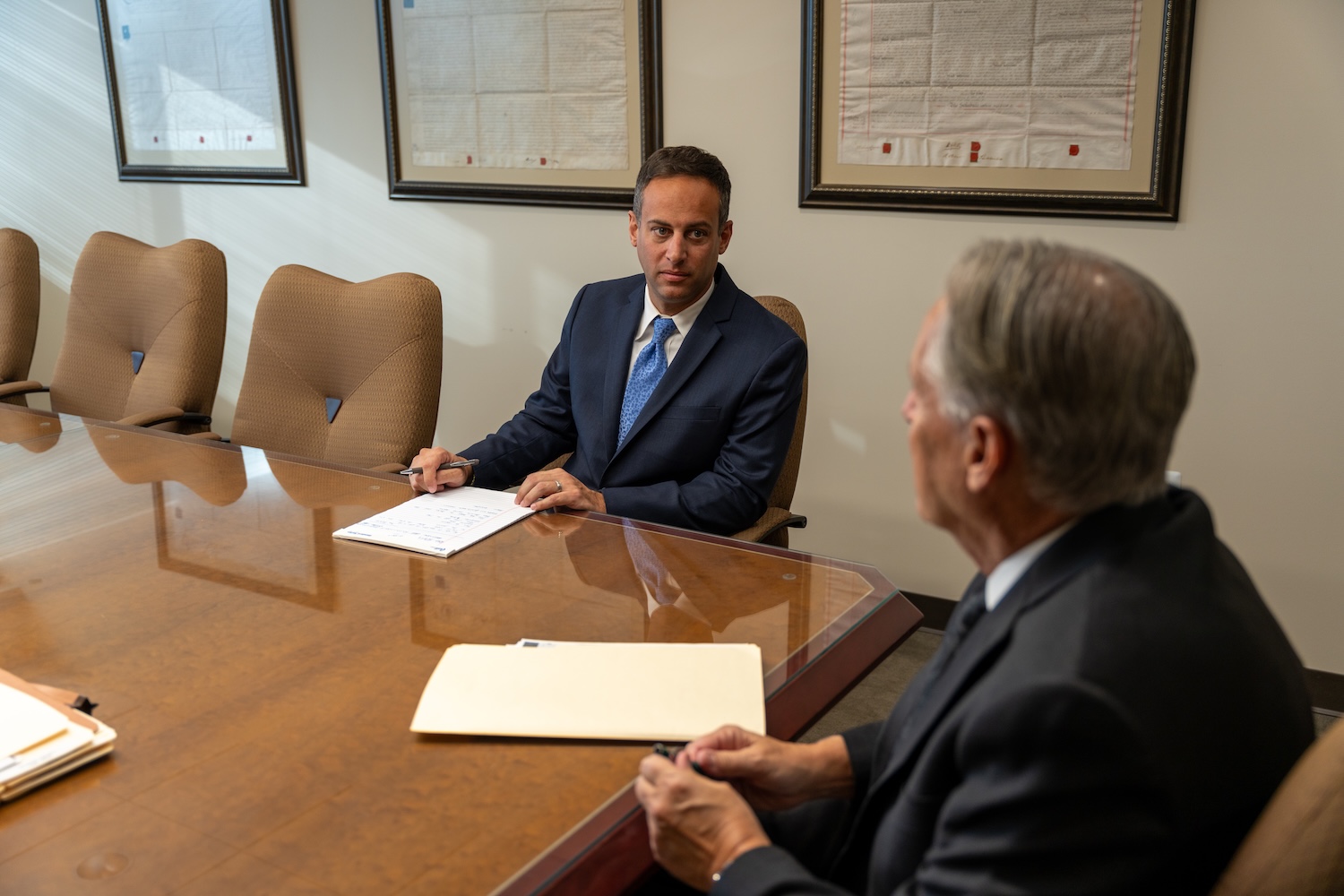Two businessmen in a conference room, discussing documents at a large wooden table.