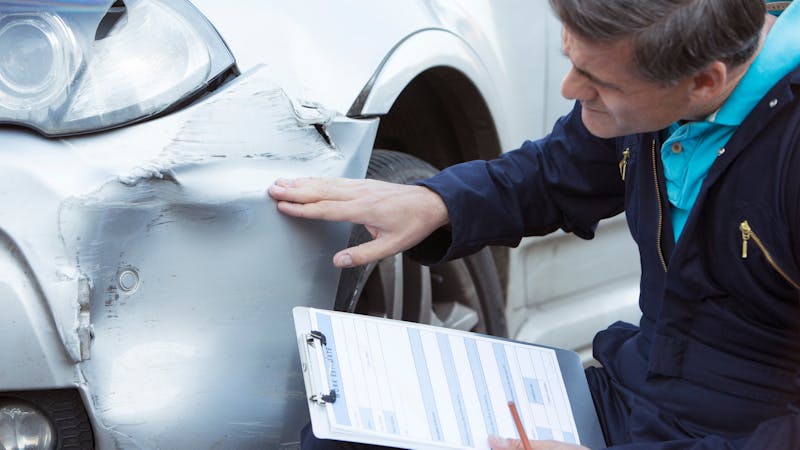 Mechanic assessing car damage with clipboard for insurance report.