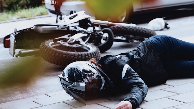 | Matz Injury Law Motorcycle accident scene with rider on ground in helmet and protective gear, bike tipped over on street.