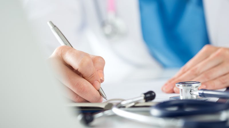 Marquette Car Accident Lawyers | Matz Injury Law A healthcare professional is writing on a clipboard next to a stethoscope, suggesting a medical context, likely in a clinic or hospital.