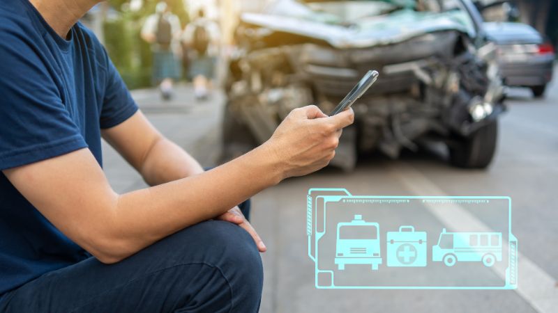 | Matz Injury Law A person squats, using a smartphone, near a car accident; icons suggest emergency calls. The context shows a street scene with blurred walking individuals.