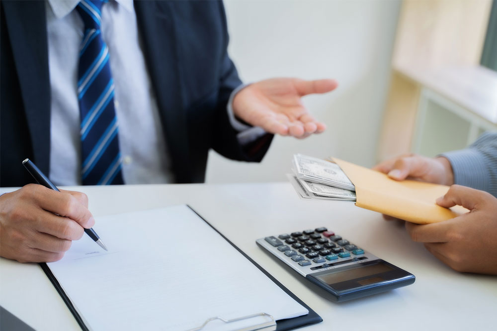 | Matz Injury Law Two people engage in a financial transaction; one hands an envelope filled with cash, while the other writes on a document. A calculator lies nearby on a desk.