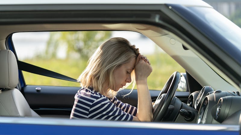 woman stressed out sitting behind the wheel of her car