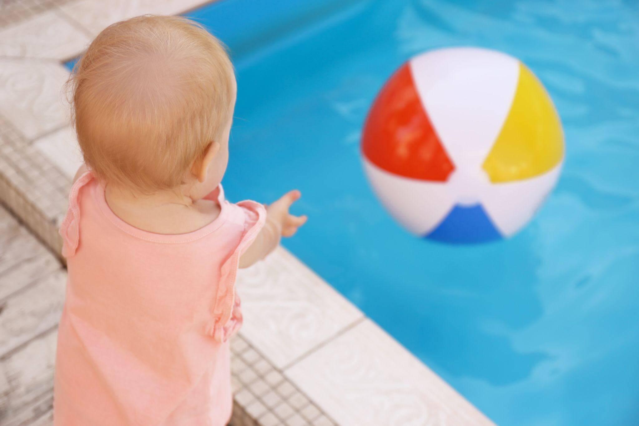 a baby standing in front of a pool with a beach ball