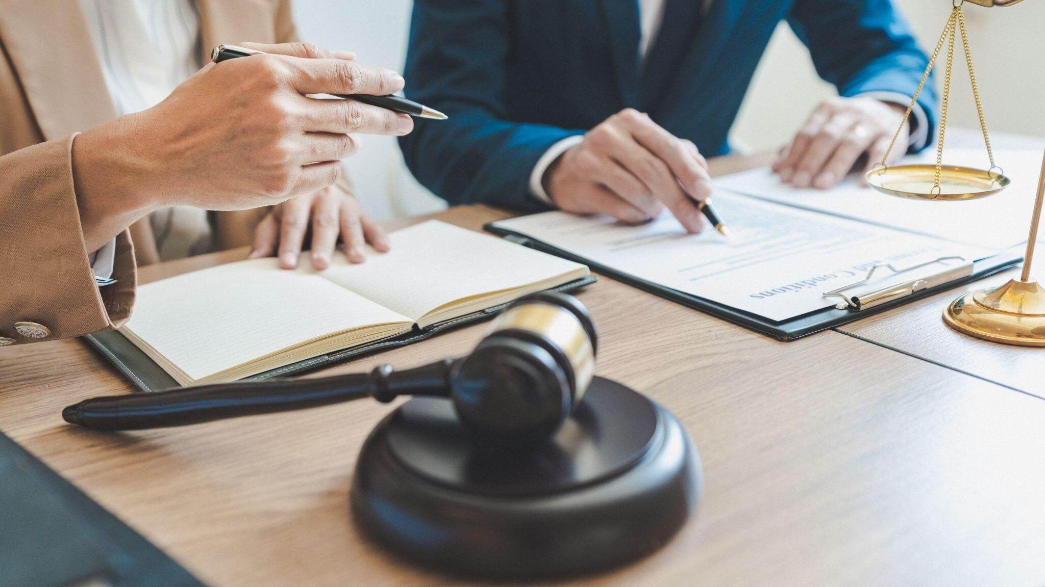 a couple of people sitting at a table with a gavel, they are reviewing legal documents