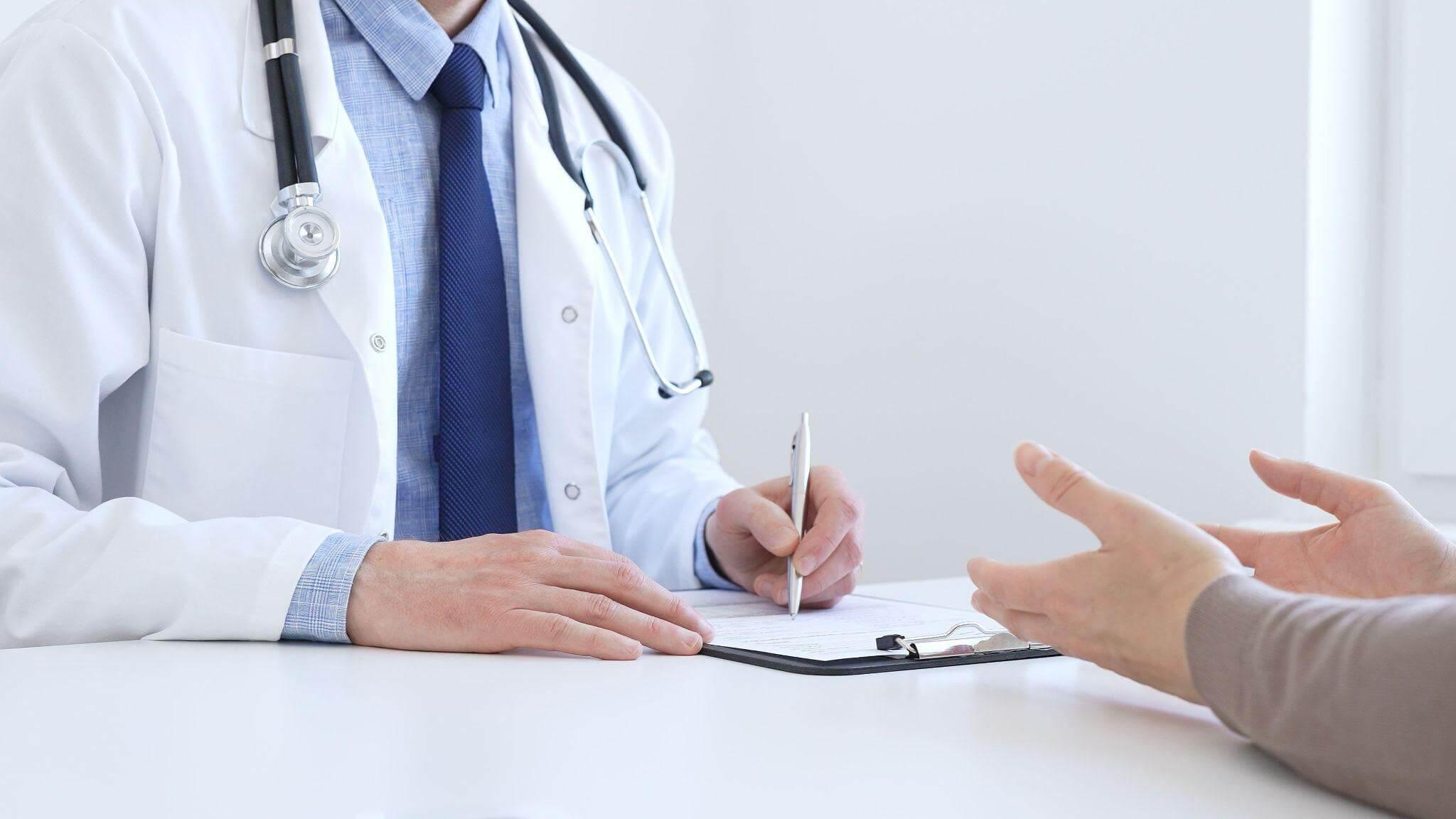 a doctor and a patient sitting at a table, the doctor is taking notes about the symptoms the patient is describing
