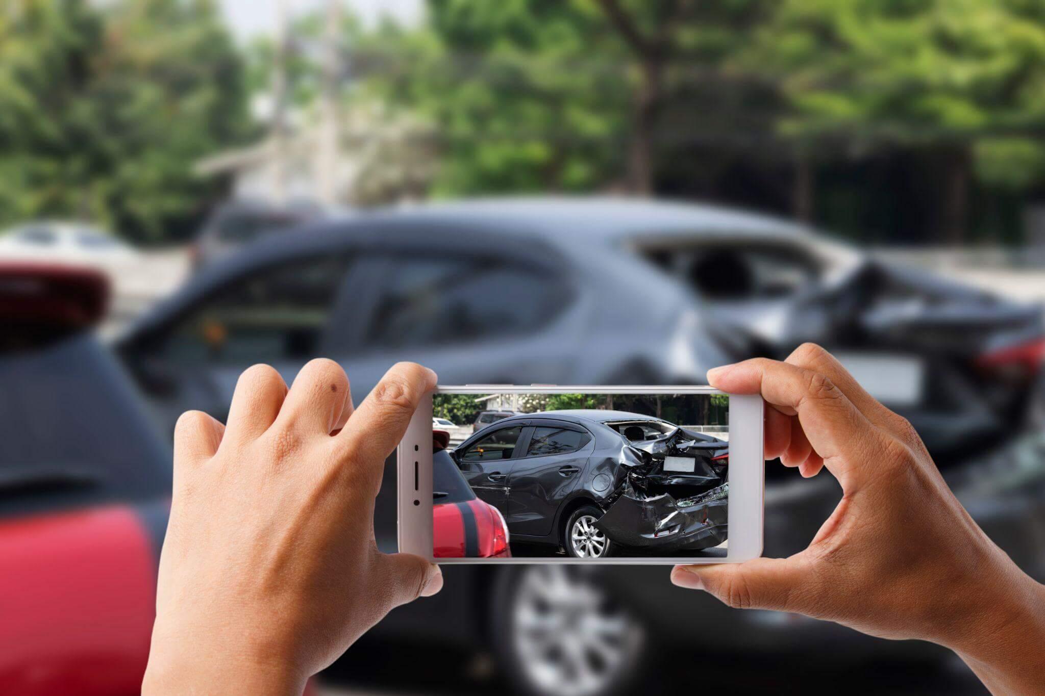a person taking a picture of a car in a parking lot, the back of said car seems to recently have been crashed