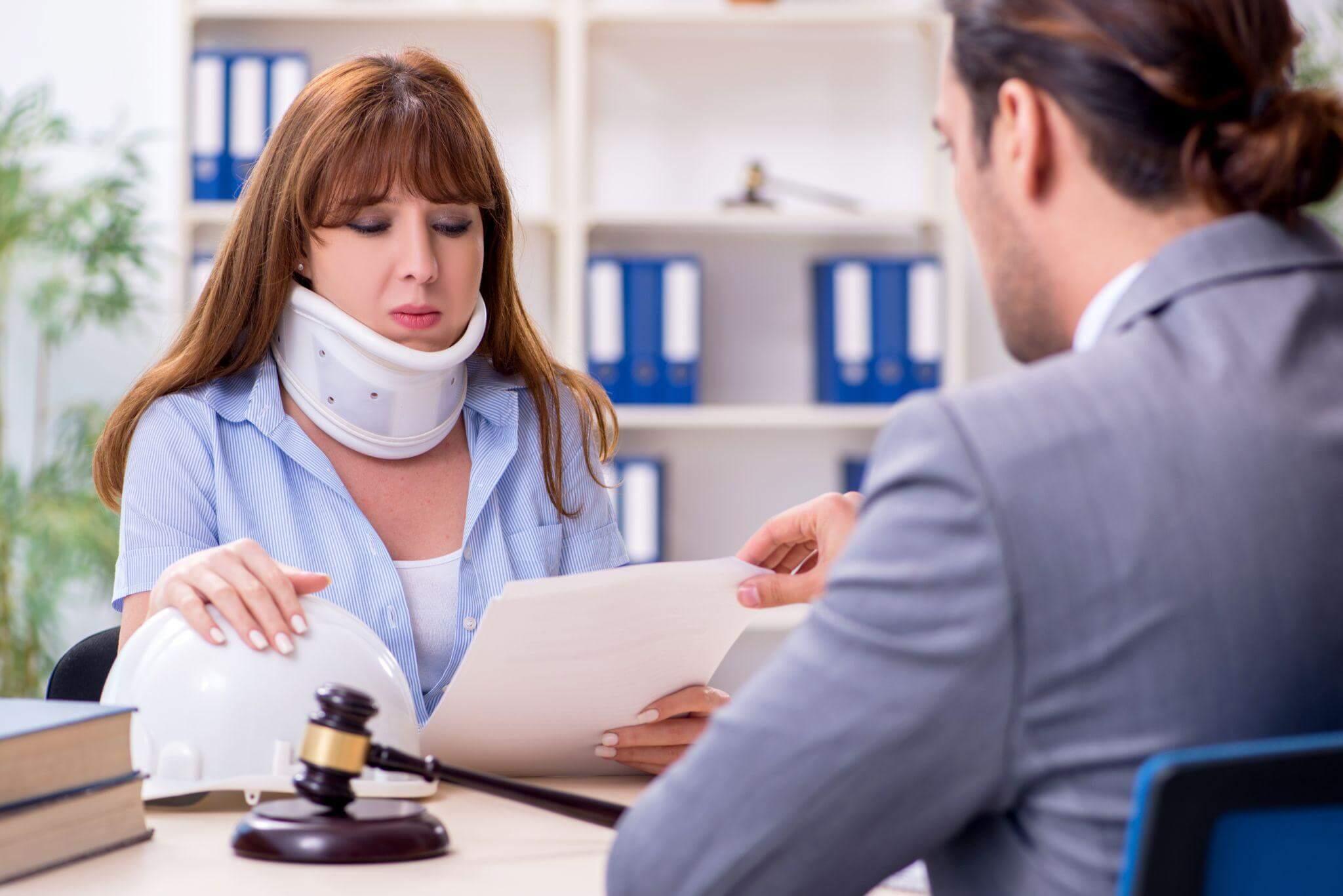 a woman in a neck brace sitting at a desk, she is reviewing legal documents with another person and the setting seems to be somber