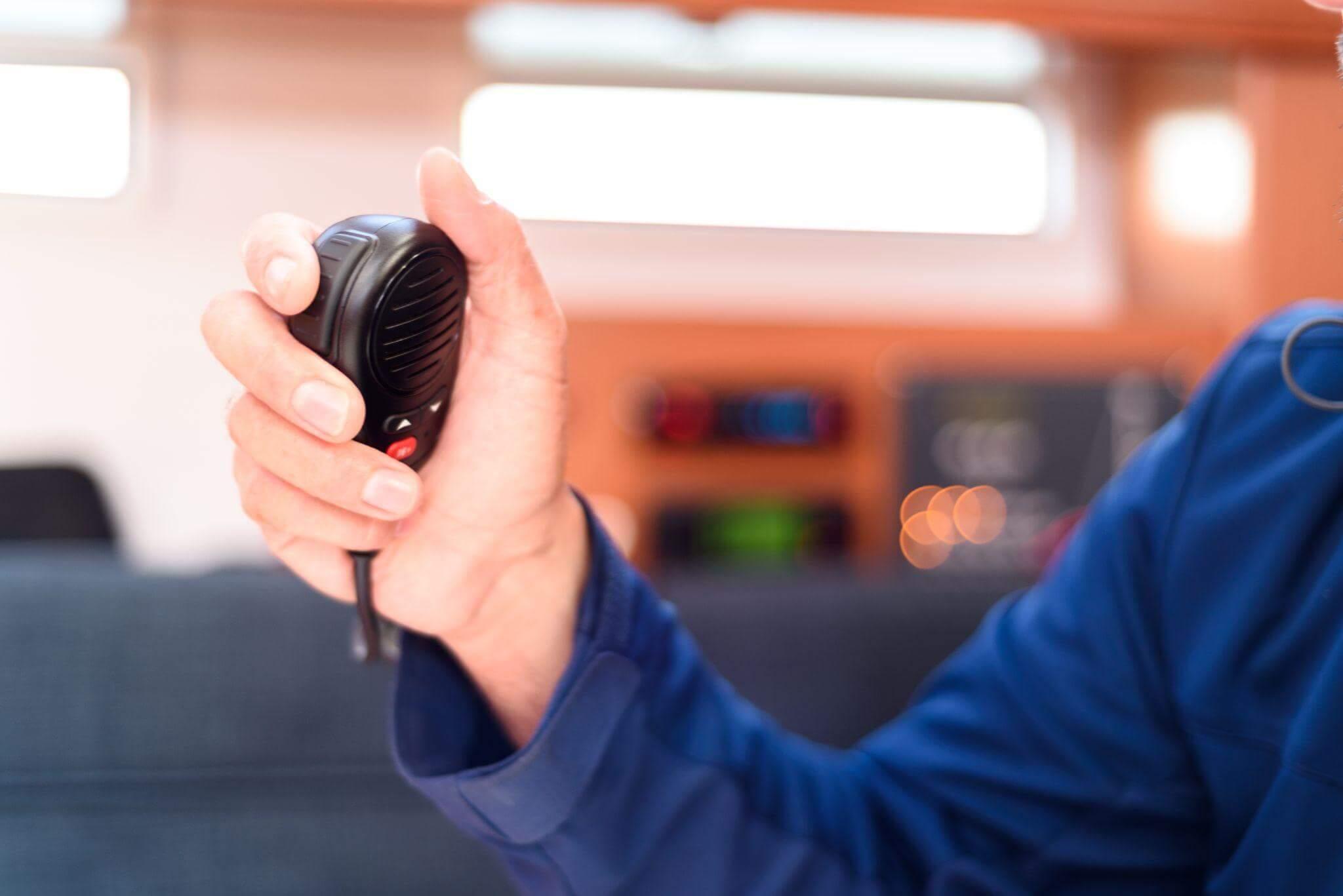 Man holding a portable radio receiver, the background is blurry but it indicates the person is inside a boat