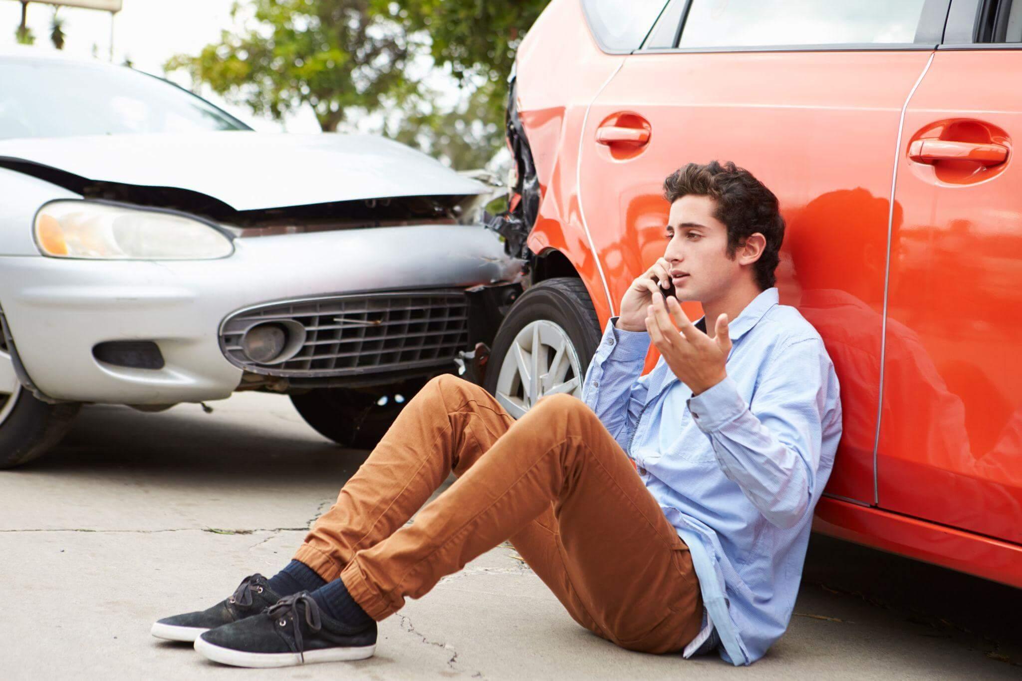 Man sitting next to car on phone after accident