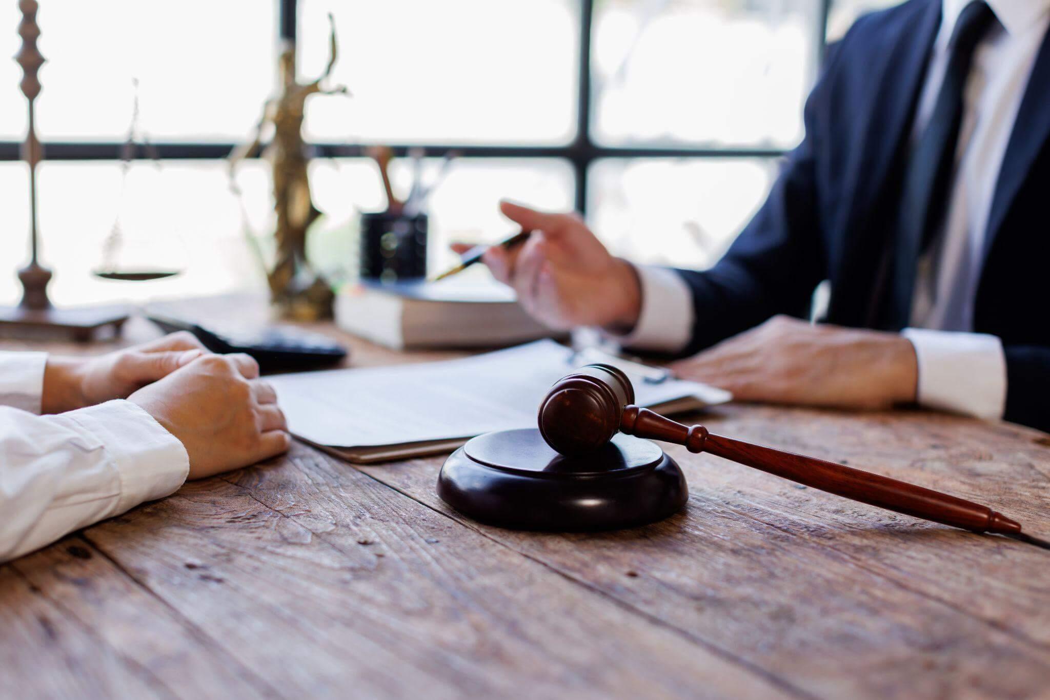 two people sitting at a table discussing a legal matter, there are papers and a gavel on the desk
