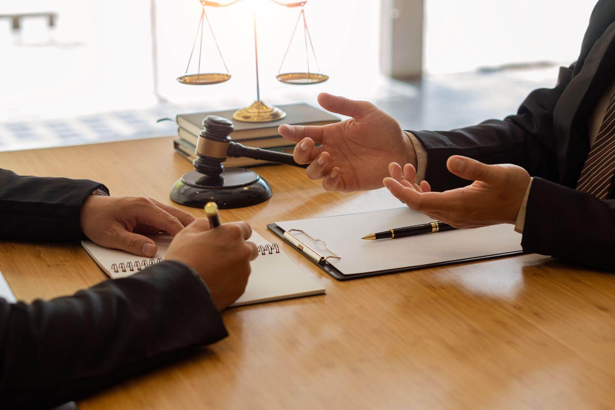 A couple of people having a meeting at a table, there's a scale of justice and a gavel next to them