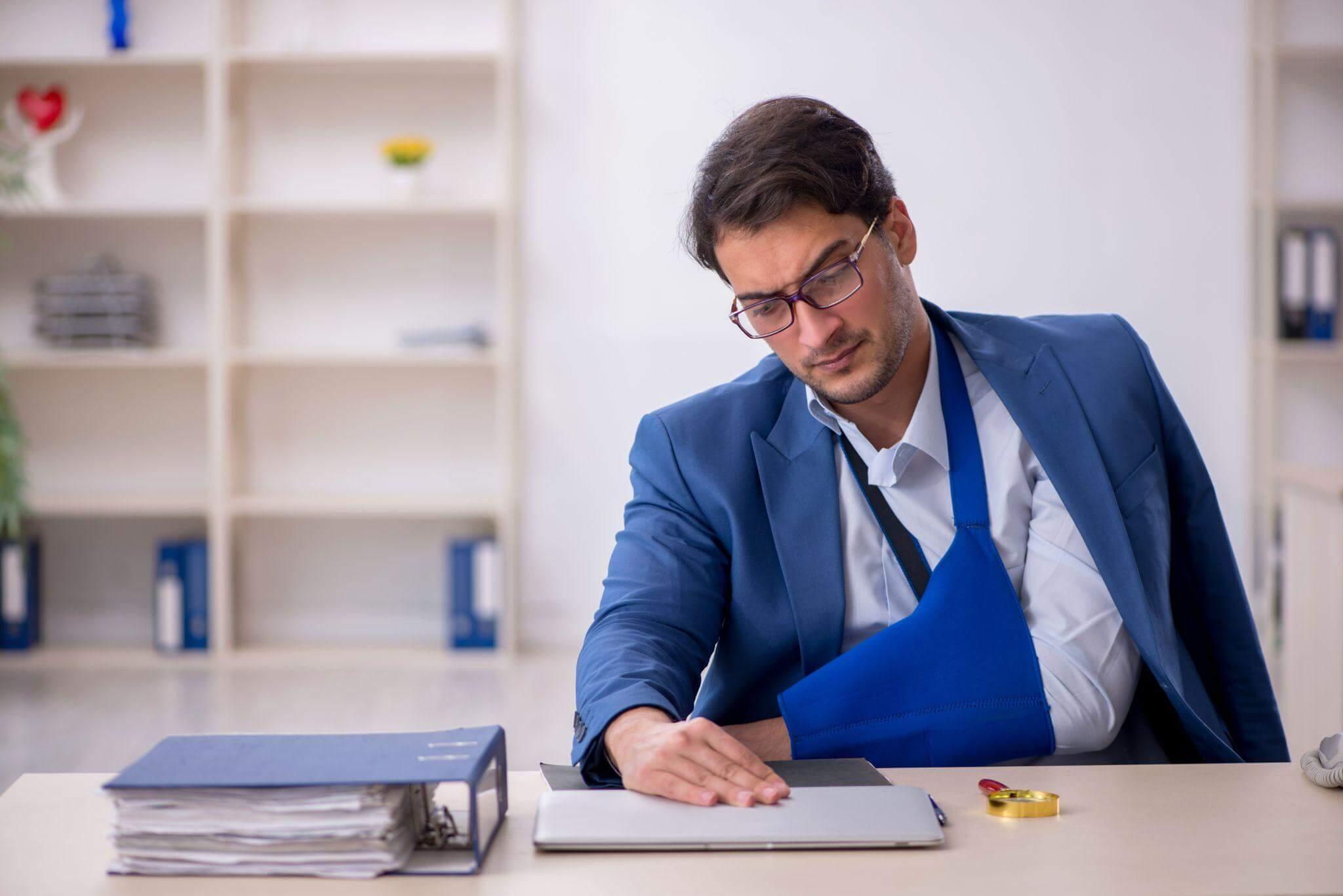 man reviewing a set of papers on a desktop, he is wearing glasses, an arm brace and a blue suit