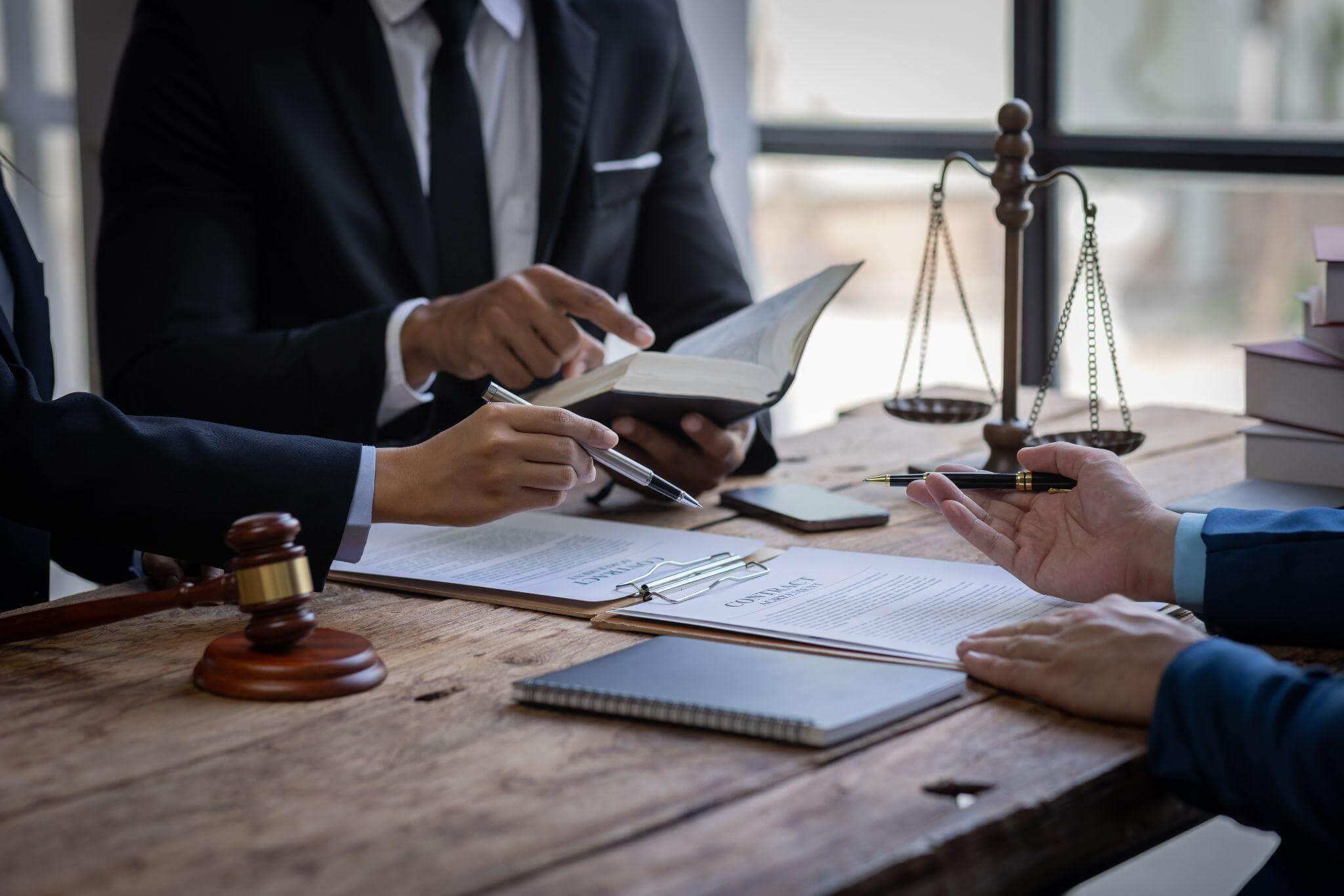 People sitting at a wooden table reviewing notes and books, all of them are wearing suits