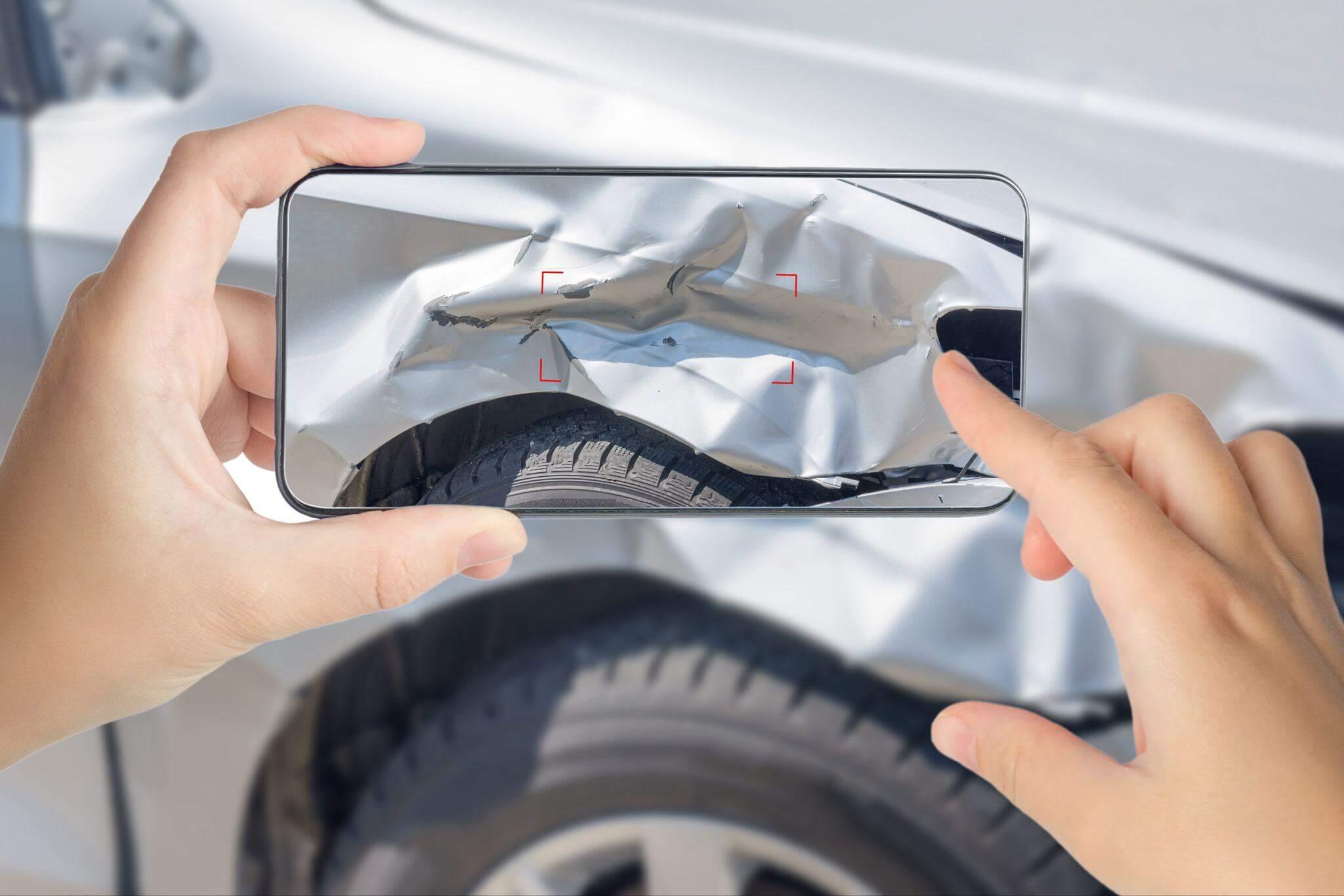 Person photographing car with smartphone, the car shows a visible dent