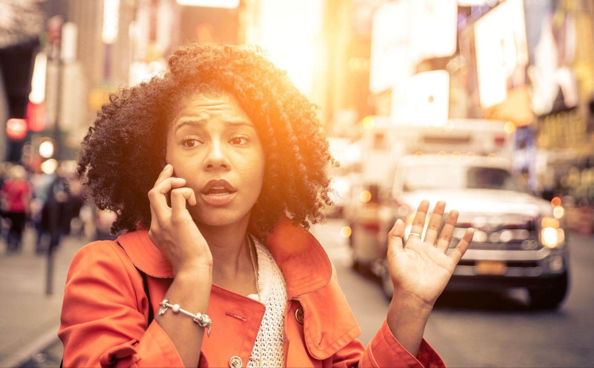 Woman on phone in city street, there's an ambulance arriving in the background