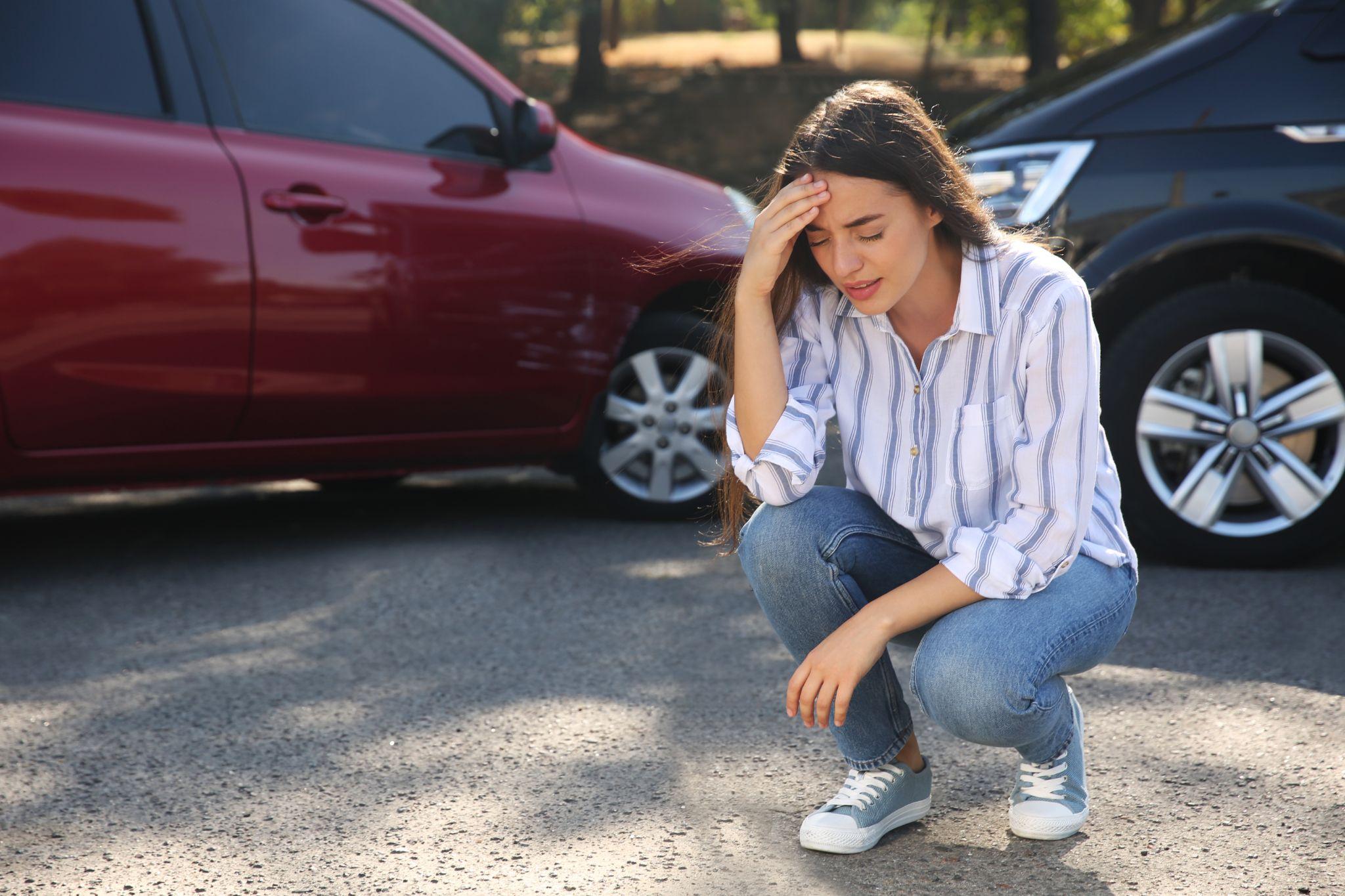 Woman sitting beside red car on ground after a car crash