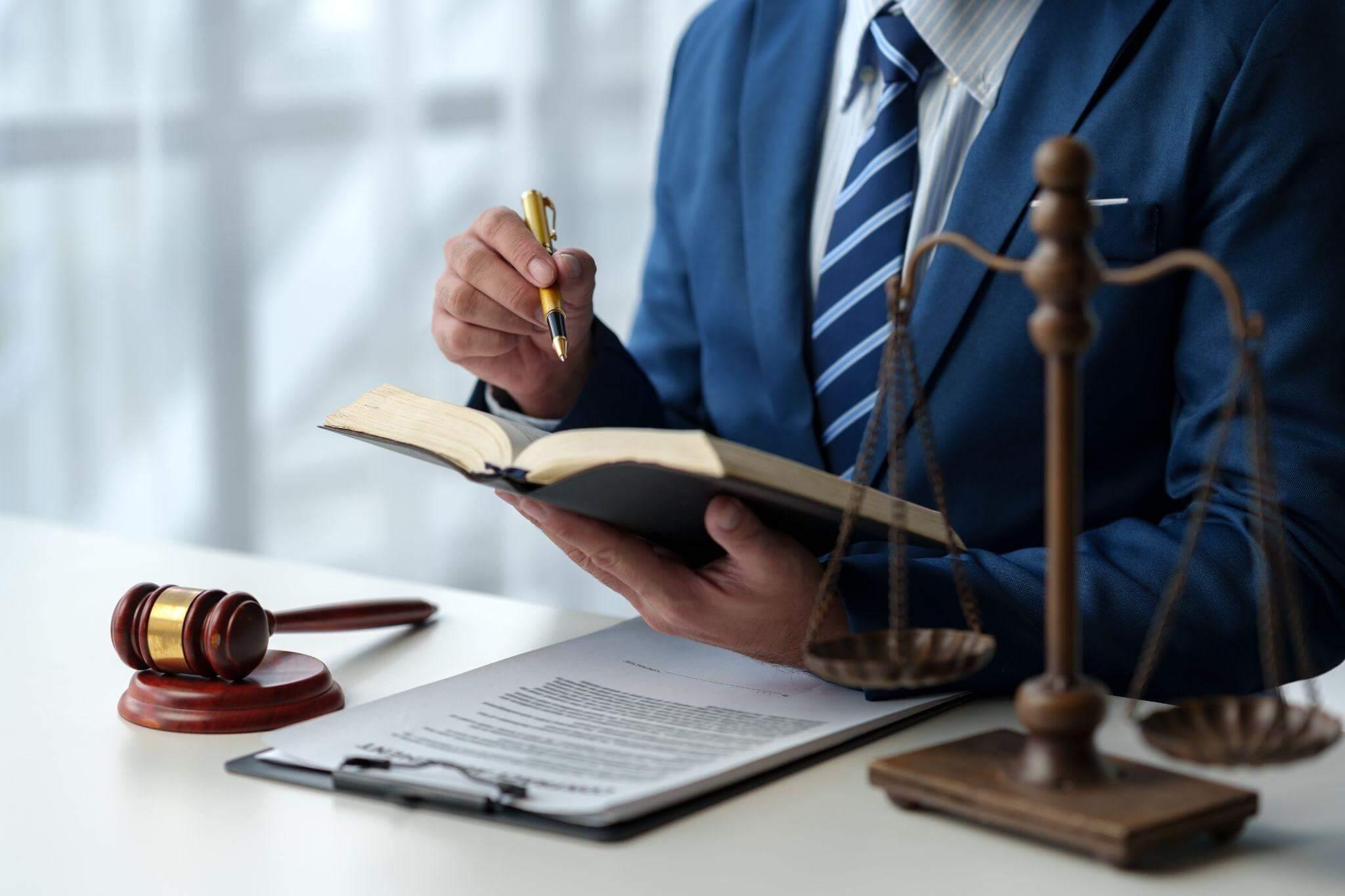 a man in a suit writing on a book next to a judge's gavel